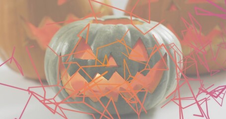 Glowing carved pumpkin on pale table, casting inner glow with pink-orange lines, blurred pumpkins