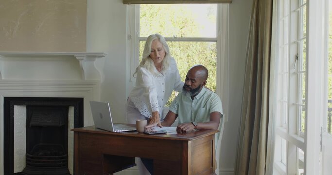 Pointing senior woman, man in white blouse, green shirt, reading papers in study with laptop
