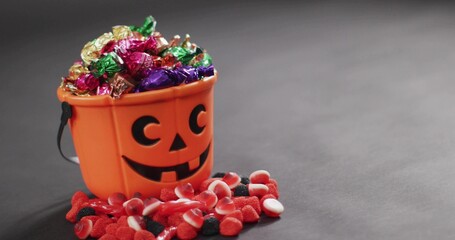 Sitting orange pumpkin bucket on gray table, holding foil candies and scattered gummies, copy space © vectorfusionart