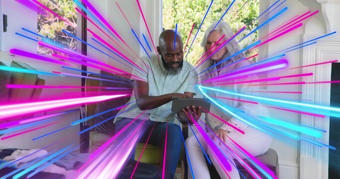Holding tablet, senior couple leaning toward screen in living room, neon streaks radiating