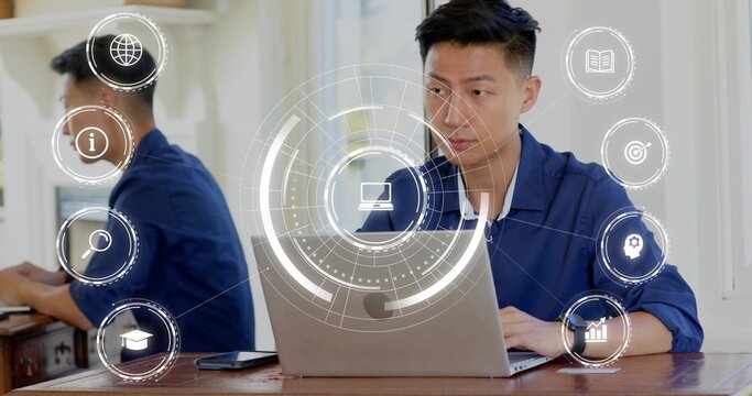 Working Asian man in navy shirt typing on laptop in home office, with smartphone, mirror, HUD