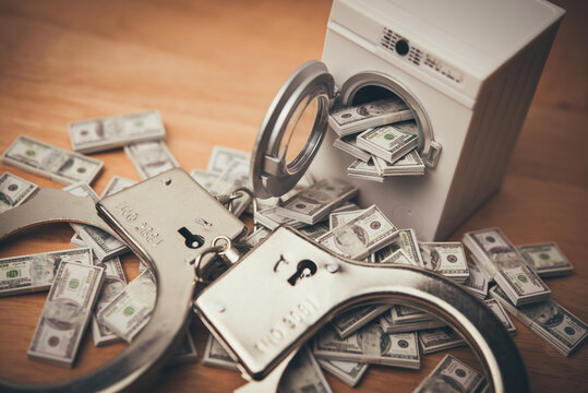 Washing machine is cleaning many US dollar bill banknotes with police handcuffs. Money laundering from scam, criminal activity, corruption, etc. or law and enforcement concept.
