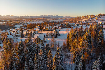 Golden hour sunrise view over the snowy village of Białka Tatrzańska in December, with the warm light illuminating the forest, traditional architecture, and the majestic Tatra Mountains.