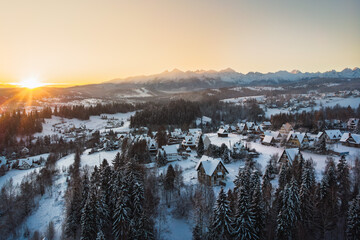 Golden hour sunrise view over the snowy village of Białka Tatrzańska in December, with the warm light illuminating the forest, traditional architecture, and the majestic Tatra Mountains.