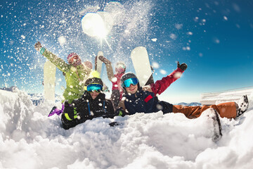 Group of happy young friends skiers and snowboarders are having fun and throwing snow while relaxing and posing together in snowdrift