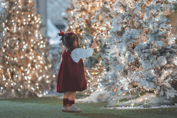 Excited little girl pointing at glowing Christmas tree lights, festive holiday atmosphere, warm family moment, childhood wonder and joy during Christmas celebration