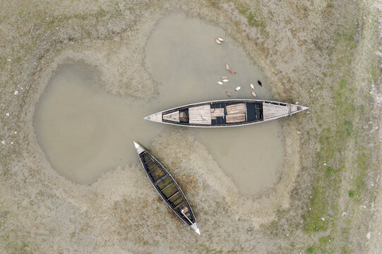 Aerial view of two rustic boats lie stranded amidst a parched landscape, mirroring the sky's muted palette, Bogura, Rajshahi Division, Bangladesh.