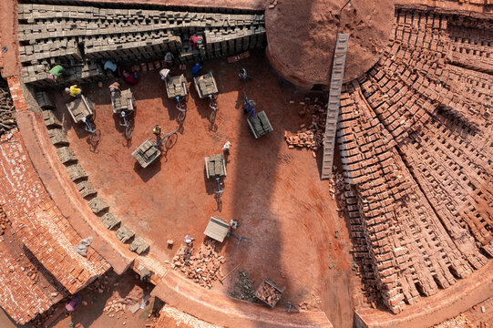 Aerial view of brick workers amidst the patterned layout of bricks, the circular kilns, and the earthy tones of the brickyard, Bogura, Rajshahi Division, Bangladesh.