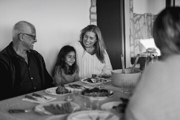 Happy latin family having fun eating lunch together during winter season - Latin female child and grandparents enjoy meal - Holiday and lifestyle concept - Black and white editing
