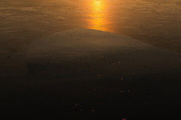 Tekstura lodu z naturalnymi wzorami rozświetlona ciepłym światłem zachodzącego słońca. Złota poświata podkreśla delikatne pęknięcia i struktury, tworząc abstrakcyjną i nastrojową zimową scenerię.