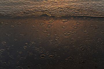 Tekstura lodu z naturalnymi wzorami rozświetlona ciepłym światłem zachodzącego słońca. Złota poświata podkreśla delikatne pęknięcia i struktury, tworząc abstrakcyjną i nastrojową zimową scenerię.