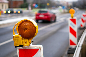 Warning signal lamp on a winter road positioned by barriers marking roadworks, with passing vehicles blurred in background