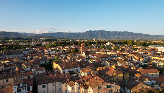 Fototapeta Aerial view of terracotta rooftops blanketing the ancient city under a vast sky, with mountains painting the horizon, Lucca, Tuscany, Italy.