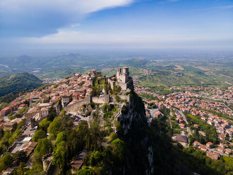 Aerial view of the fortress standing boldly atop Monte Titano, surrounded by the ancient walls of San Marino, casting shadows on the quaint town below, San Marino, San Marino.