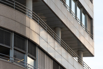 Modern commercial building facade with metal railings, vertical columns and shaded windows creating strong geometric lines and contemporary design