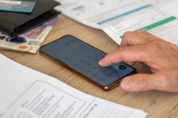 A close up of a person using a phone calculator to add up the cost of household utility bills. A...