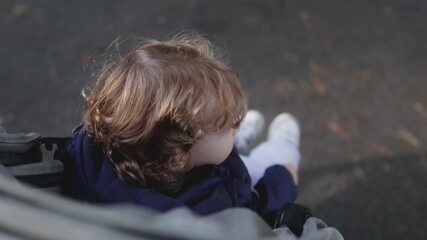 Toddler looking outward from stroller during outdoor walk creating gentle candid moment filled with quiet curiosity natural movement fresh air and relaxed family outing on cool neighborhood day