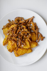 Delicious oven baked potatoes with chanterelle mushrooms served on a white plate. Top down food shot for recipe blogs, cooking magazines, or restaurant menus. Rustic comfort food at its best.
