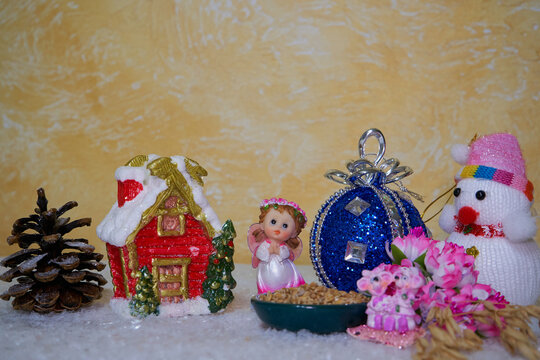 New Year's composition: toy house and snowman on white artificial snow, Small angel figurine with pink wings, prosperity and Christmas comfort