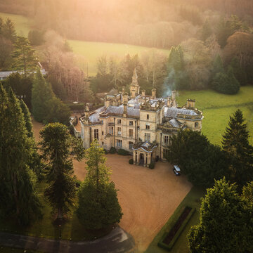 Aerial view of a stately building enveloped by emerald grounds and a veil of mist, the stone architecture contrasts with the soft, diffused light, Bala, Wales, United Kingdom.