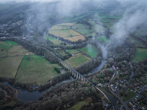 Aerial view of the River Dee snaking through verdant fields and around the Pontcysyllte Aqueduct under a blanket of low-hanging clouds, Llangollen, Wales, United Kingdom.