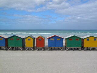 Naklejka premium Iconic colorful Muizenberg beach huts on the sandy coast of False Bay, Cape Town.