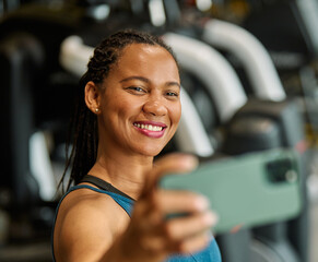 Portrait of a young black woman using a phone ana making a selfie photo, taking a break exercising in a gym, running using  thereadmill machine equipment, healthy lifestyle and cardio exercise at fitn