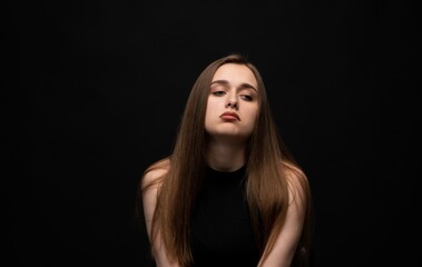 Moody young woman posing with tilted head in low-key studio portrait on black background with soft shadows