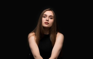 Fototapeta premium Calm studio portrait of a young woman with neutral facial expression against a dark background