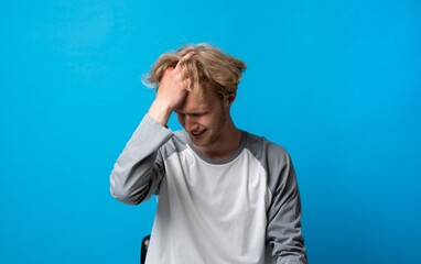 Stressed young man holding his head in discomfort on blue background, headache and frustration concept