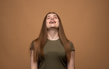 Joyful young woman laughing with head raised, expressive positive emotion portrait on warm studio background