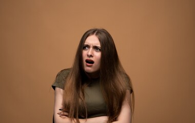 Confused shocked young woman reacting with open mouth, expressive emotional portrait on warm studio backdrop