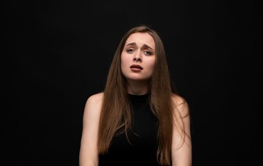 Sad young woman with worried facial expression in dramatic emotional studio portrait on dark background