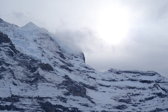 Bright winter sunlight breaking through clouds above a snowy Swiss mountain ridge near Kleine Scheidegg, highlighting the rugged icy textures and dramatic alpine landscape.