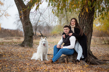 A young family - a guy, a girl and a cute fluffy Samoyed - are walking by the river