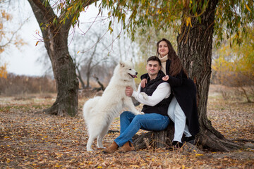 A young family - a guy, a girl and a cute fluffy Samoyed - are walking by the river