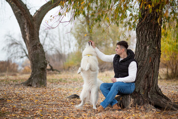 A guy trains his pet Samoyed while sitting in a park by the river