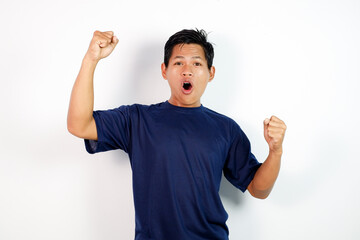 Happy Young Man In Blue T‑Shirt Celebrating Victory With Raised Fists and A Wide Open Mouth, Energetic Expression.