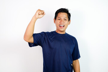 Happy Young Man In Blue T‑Shirt Celebrating Victory With Raised Fists and A Wide Open Mouth, Energetic Expression.