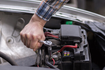 Naprawa akumulatora samochodowego – męska dłoń dokręcająca klemę kluczem w komorze silnika