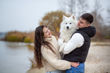 A family - a young man and a girl holding a cute fluffy Samoyed on the banks of the Dnieper River