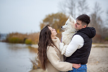 A family - a young man and a girl holding a cute fluffy Samoyed on the banks of the Dnieper River