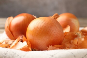 Fresh onion bulbs with peels on kitchen towel, closeup
