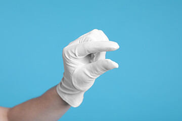Woman in cloth glove showing size of something on light blue background, closeup