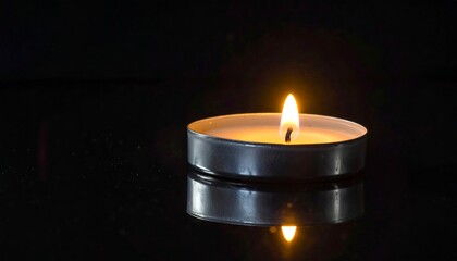 A small candle with a bright flame sits on a glossy surface reflecting the light against a dark backdrop