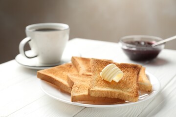 Fresh toasted bread slices served with butter, jam and tea on white wooden table, closeup