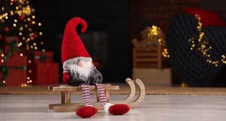Obraz premium Funny Christmas gnome on wooden sleigh in decorated room. Space for text