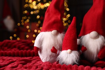 Obraz premium Funny Christmas gnomes on red blanket in decorated room, closeup. Space for text