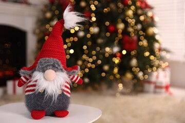 Obraz premium Funny Christmas gnome on white table in decorated room. Space for text