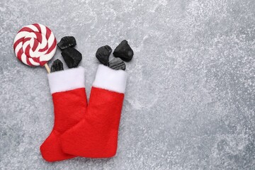 Pieces of black coal and lollipop in Christmas stockings on gray textured table, flat lay. Space...